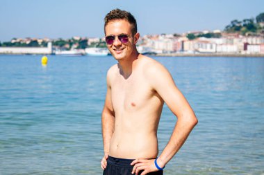 Kumsalda güneş gözlüklü yakışıklı bir genç.