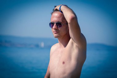 Kumsalda güneş gözlüklü yakışıklı bir genç.