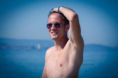 Kumsalda güneş gözlüklü yakışıklı bir genç.