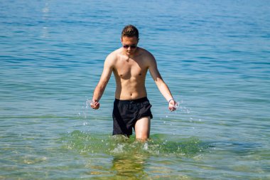 Yakışıklı genç adam sahilde okyanusta banyo yapıyor.