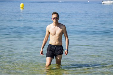 Yakışıklı genç adam sahilde okyanusta banyo yapıyor.