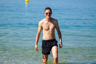 Yakışıklı genç adam sahilde okyanusta banyo yapıyor.