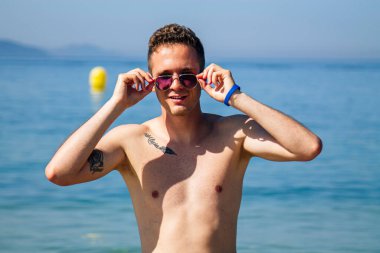 Kumsalda güneş gözlüklü yakışıklı bir genç.