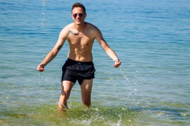 Yakışıklı genç adam sahilde okyanusta banyo yapıyor.