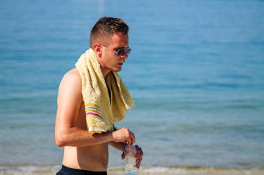 Adam egzersiz yaptıktan sonra sahilde dinlenip su içiyor.