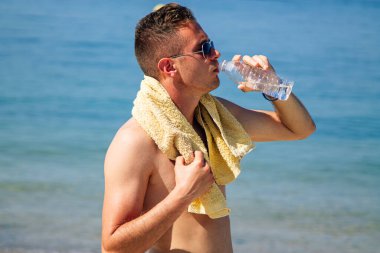 Adam egzersiz yaptıktan sonra sahilde dinlenip su içiyor.