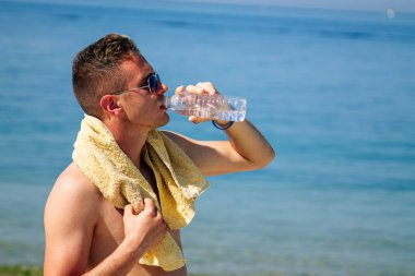 Adam egzersiz yaptıktan sonra sahilde dinlenip su içiyor.