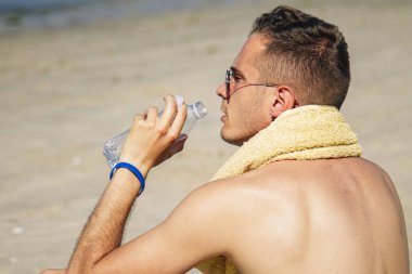 Adam egzersiz yaptıktan sonra sahilde dinlenip su içiyor.