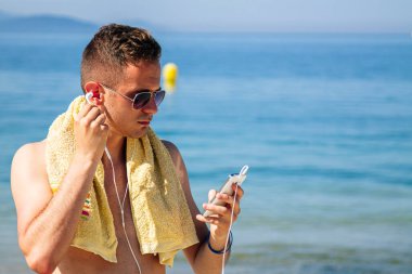 Sahilde cep telefonu ve kulaklığı olan bir adam.