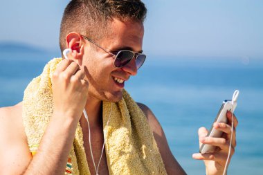 Sahildeki adam cep telefonu ve kulaklıklarla rahatladı.