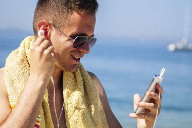 Sahildeki adam cep telefonu ve kulaklıklarla rahatladı.