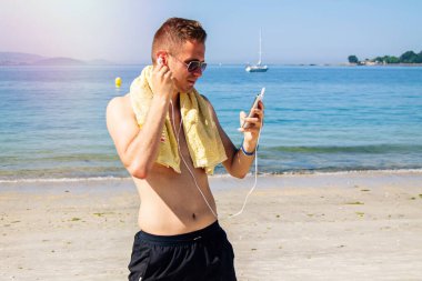 Sahildeki adam cep telefonu ve kulaklıklarla rahatladı.