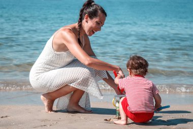 Anne kumsalda oğluyla kumdan kaleler yapıyor.