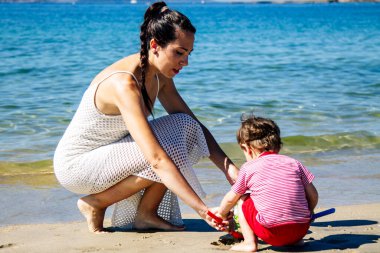 Anne kumsalda oğluyla kumdan kaleler yapıyor.