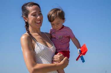 Kumsalda oğlu kollarında gülümseyen bir anne.