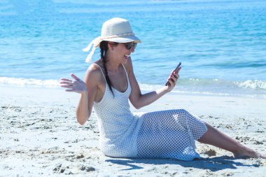 Sahilde cep telefonuyla sürpriz jestler yapan bir kadın.