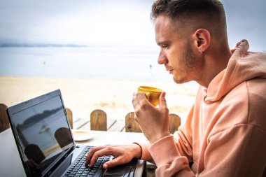 Bilgisayarlı genç adam kahve içiyor.