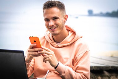 Dışarıda cep telefonu ve dizüstü bilgisayarı olan genç adam.
