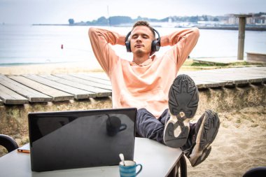 Kulaklıklı ve laptoplu rahat bir genç adam.