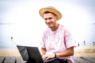 Sahilde dizüstü bilgisayar kullanan bir adam.