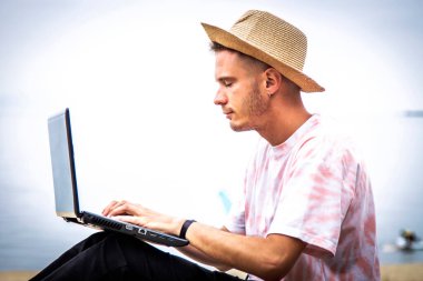 Sahilde dizüstü bilgisayar kullanan bir adam.