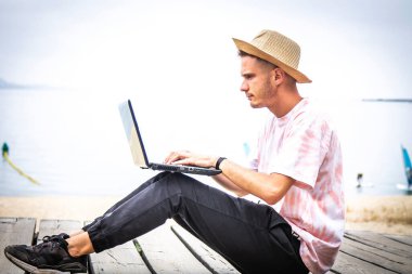 Sahilde dizüstü bilgisayar kullanan bir adam.