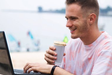 Adam kumsalda dizüstü bilgisayar kullanıyor ve kahve içiyor.