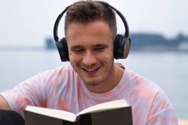 Kulaklıklı rahat bir adam kitap okuyor.