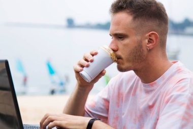 Adam dizüstü bilgisayar kullanıyor ve kahve ısmarlıyor.