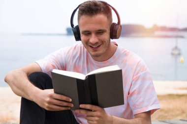 Kulaklıklı rahat bir adam kitap okuyor.