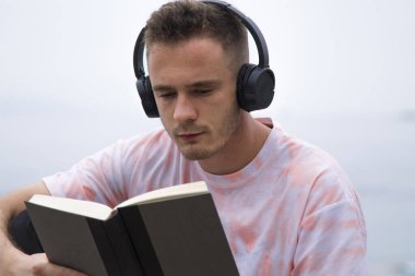 Kulaklıklı rahat bir adam kitap okuyor.