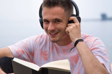 Kulaklıklı rahat bir adam kitap okuyor.