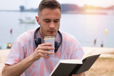 Kulaklıklı rahat bir adam kitap okuyor ve kahve içiyor.