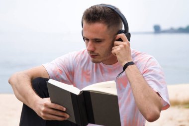 Kulaklıklı rahat bir adam kitap okuyor.