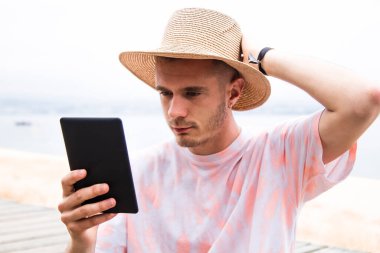 Şapkalı genç adam dışarıda dijital tablet kullanıyor.