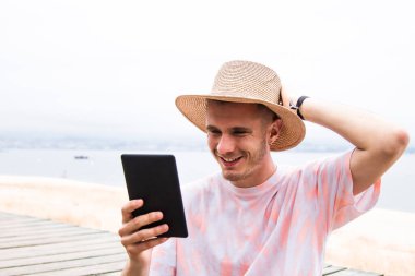 Şapkalı genç adam dışarıda dijital tablet kullanıyor.