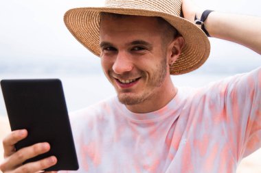 Şapkalı genç adam dışarıda dijital tablet kullanıyor.