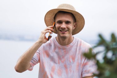 Şapkalı genç adam dışarıda cep telefonuyla konuşuyor.