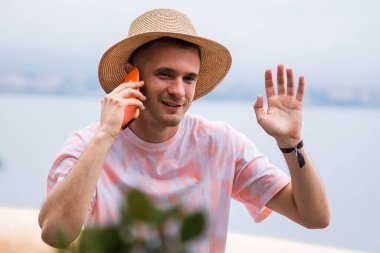 Genç adam el sallarken cep telefonuyla konuşuyor.