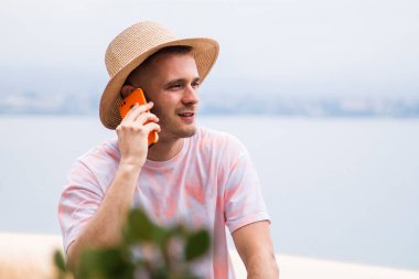 Şapkalı genç adam dışarıda cep telefonuyla konuşuyor.