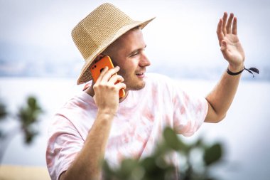 Genç adam el sallarken cep telefonuyla konuşuyor.