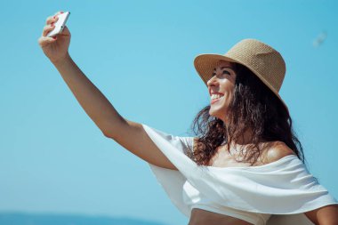 Kumsalda selfie çeken şapkalı bir kadın.