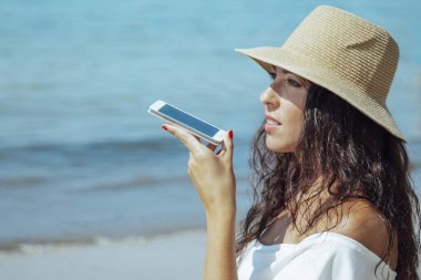 Plajda şapkalı bir kadın cep telefonuyla mesaj yolluyor.