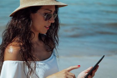 Sahilde dijital tablet ya da e-kitap kullanan genç bir kadın.