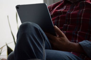 Kanepede elinde tabletle oturan adam.