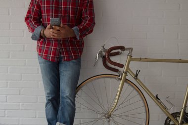 Evdeki adam bisikletin yanındaki duvara yaslanmış cep telefonuyla fotokopi çekiyor.