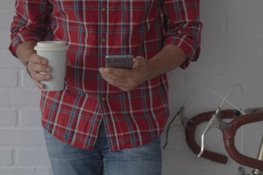 Bisikletinin yanında kahve ve cep telefonu olan hippi adam.