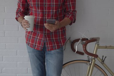 Bisikletinin yanında kahve ve cep telefonu olan hippi adam.