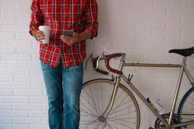 Bisikletinin yanında kahve ve cep telefonu olan hippi adam.