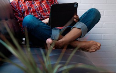 Tablet veya dizüstü bilgisayar kullanarak koltukta rahat bir adam.